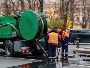 Workers in safety gear operate a Suction truck to clean a city sewer.